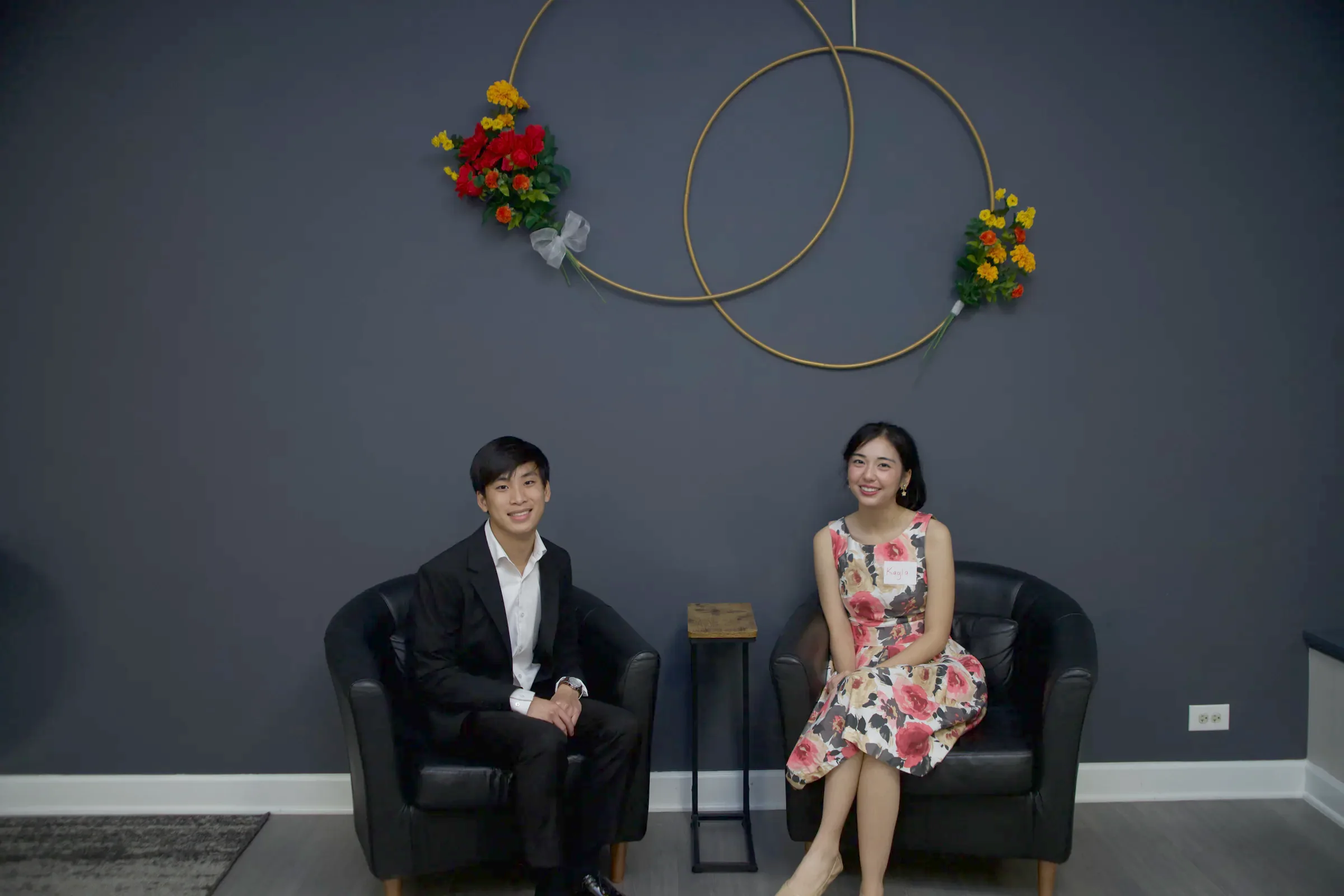 Two volunteers seated beneath a floral hoop decoration