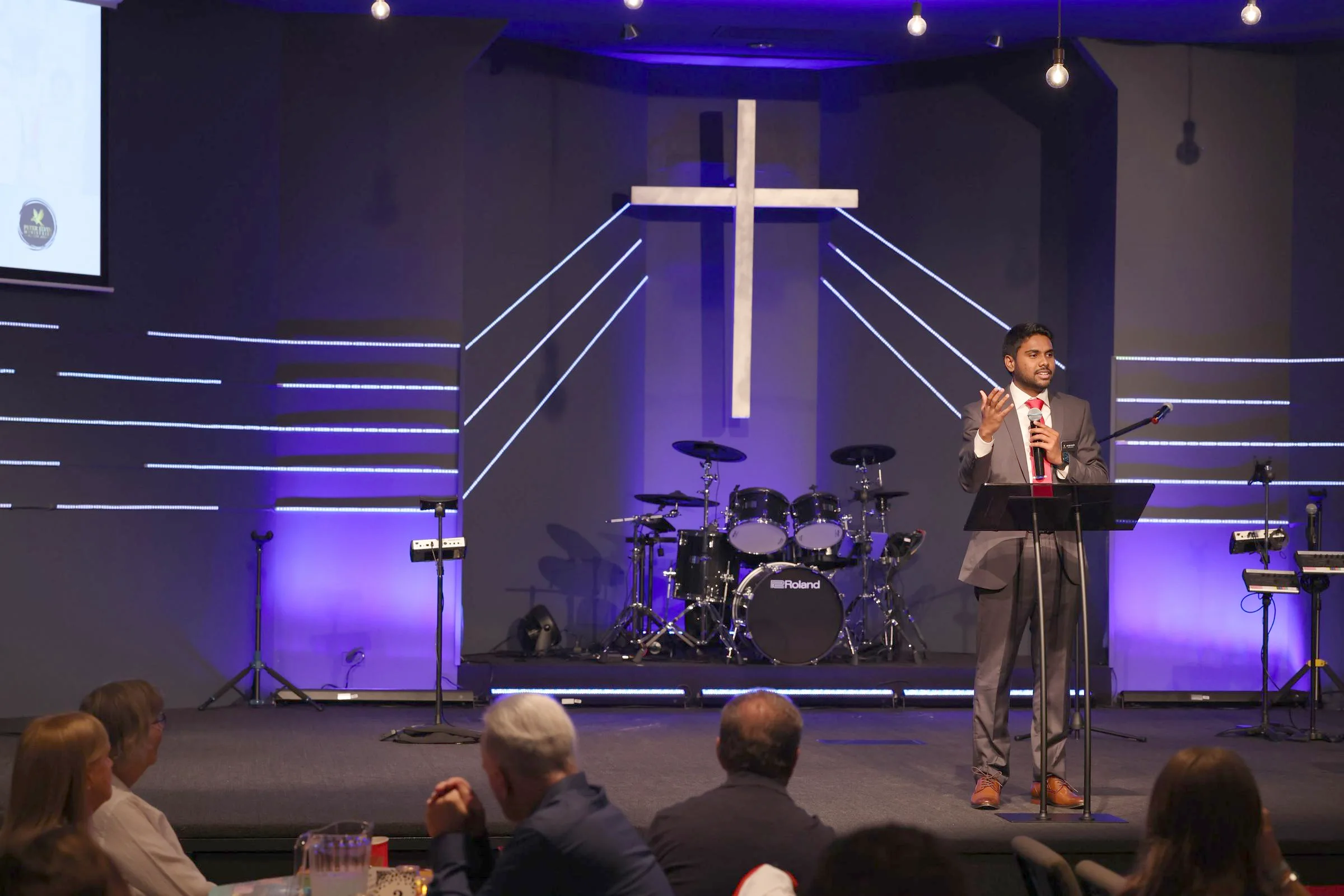 A ministry leader speaking at the podium beside the lit cross