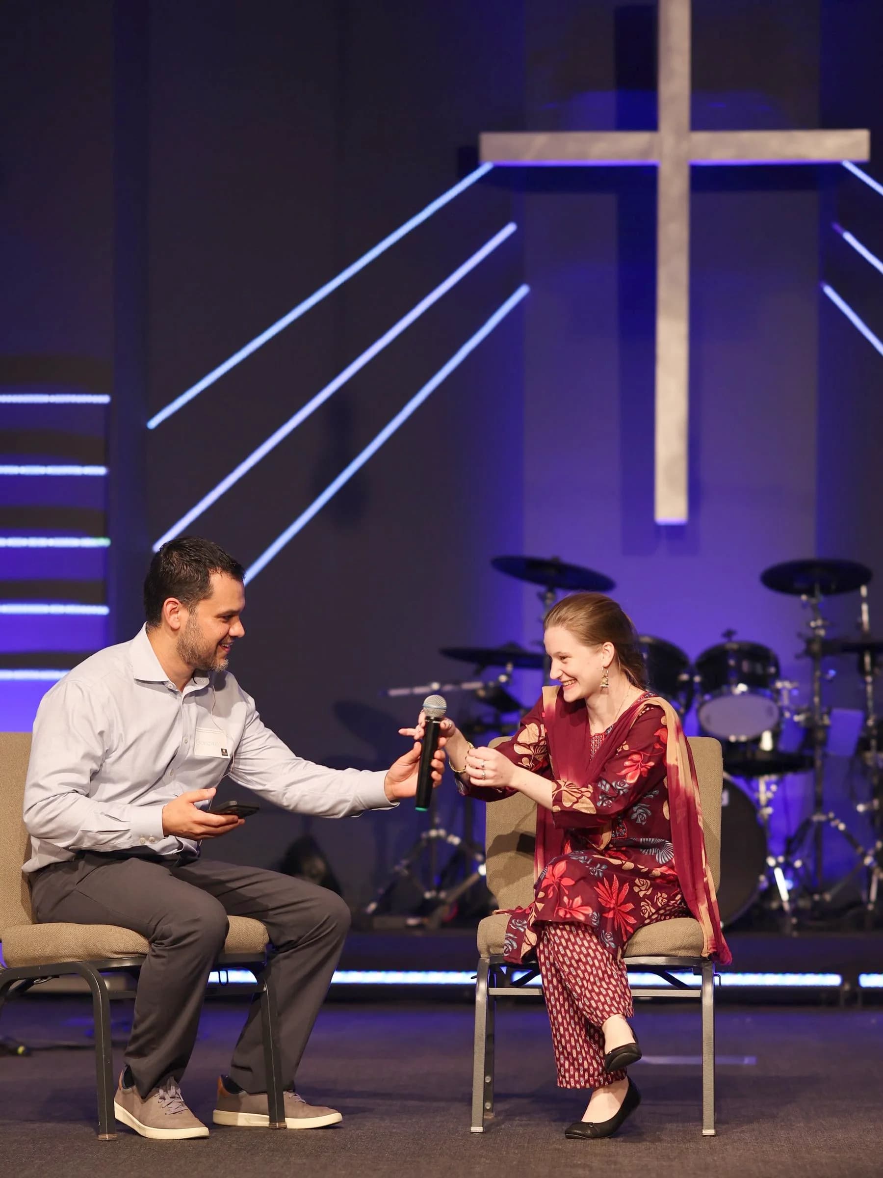 A guest being interviewed on stage beneath the lit cross