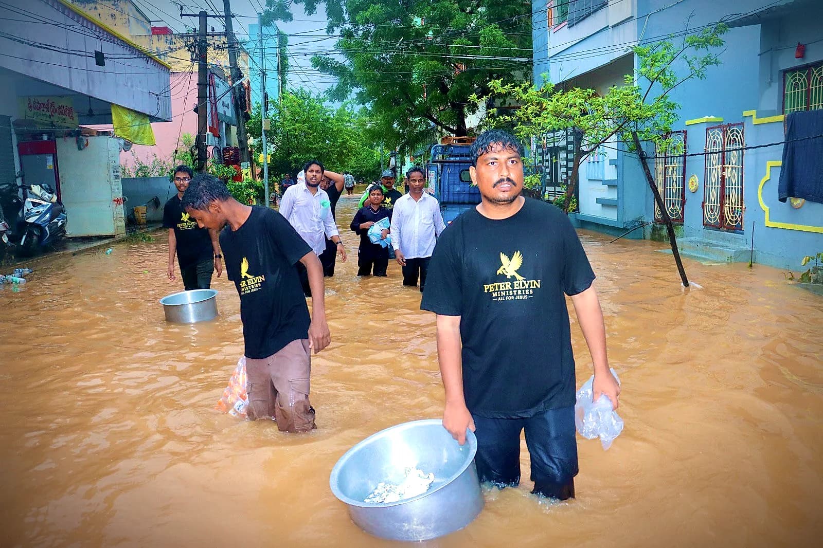 Ministry workers wading through a flooded street with relief supplies