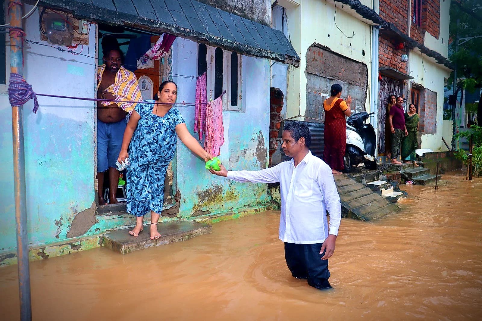 A pastor handing food to a woman at her flooded doorstep