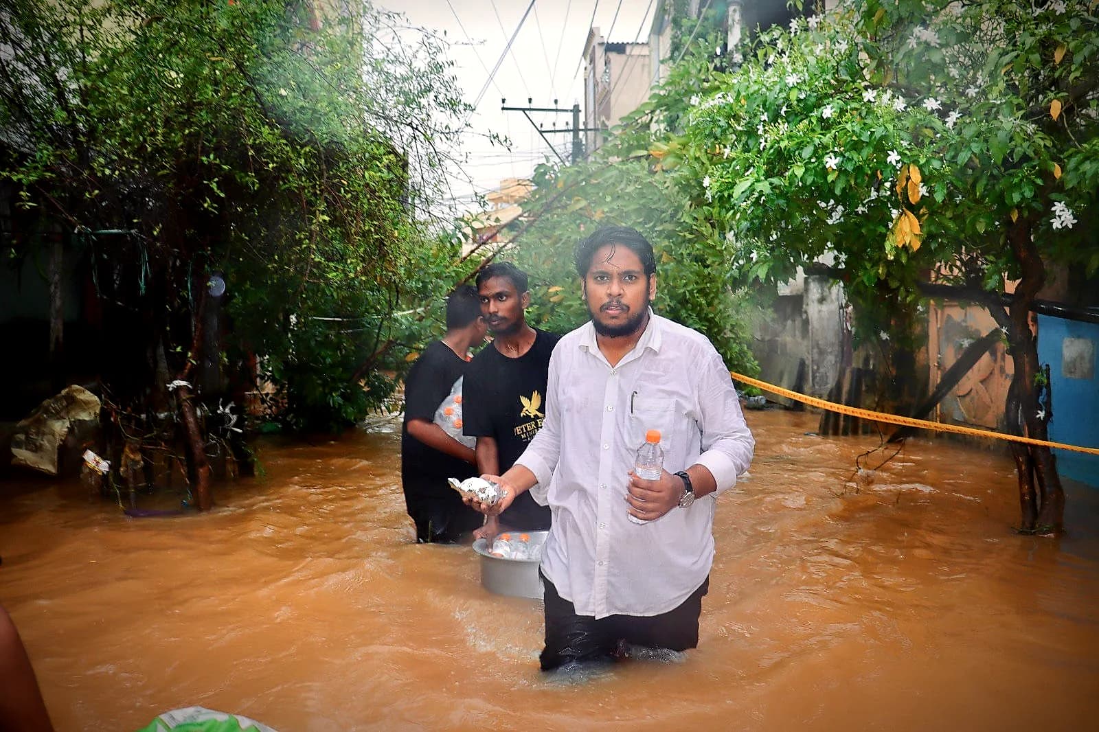 Team members carrying food packets through knee-deep floodwater