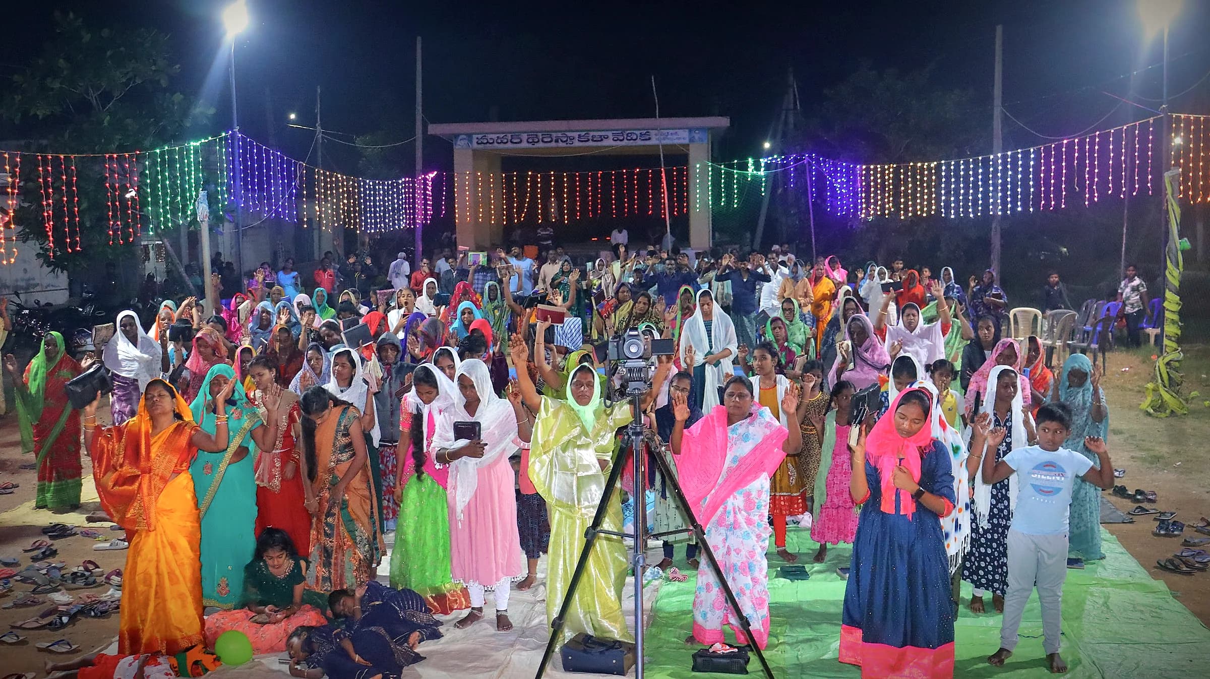 A night crusade crowd standing in worship under strings of lights