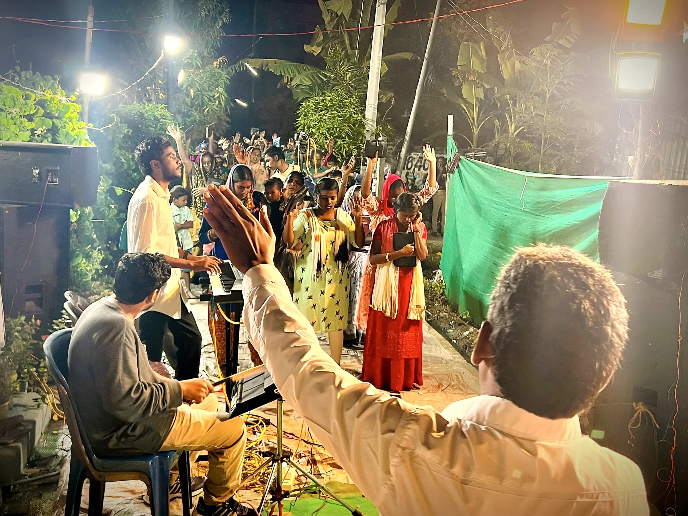 A man raising his hand in worship at a night village meeting