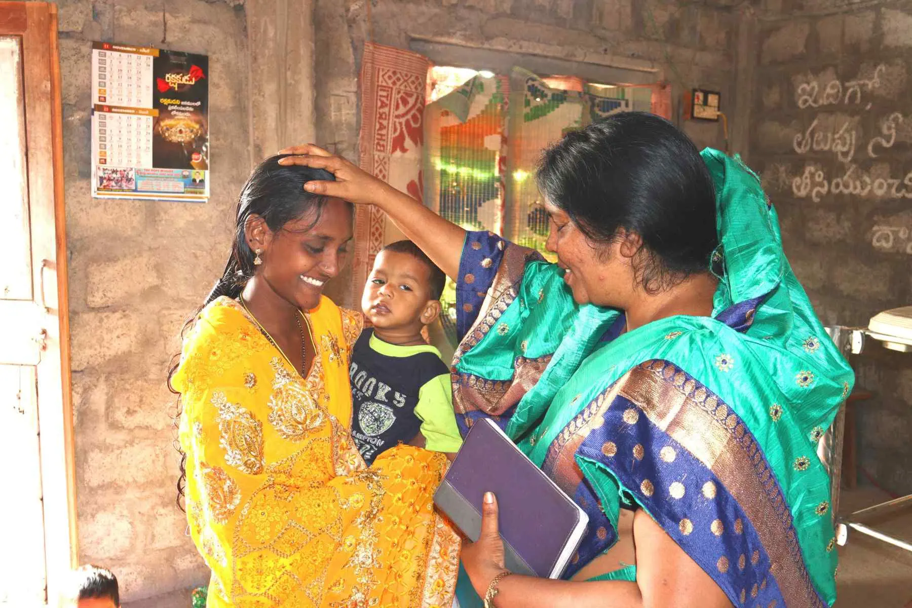 A ministry worker praying over a young mother during a home visit in India