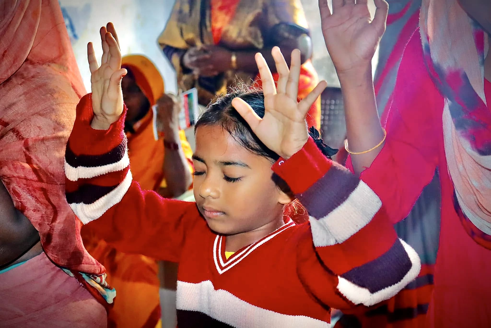 A young girl with eyes closed and hands raised in worship