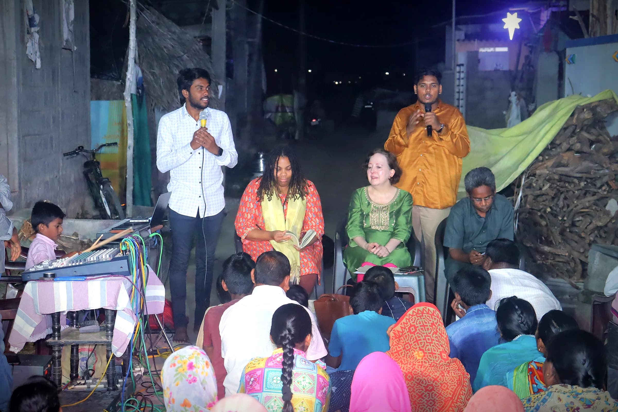 A night street meeting with speakers and seated villagers